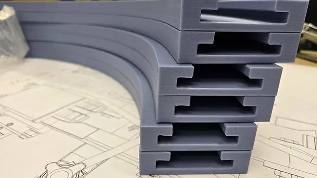 Stack of machined wear strips resting on a conveyor assembly drawing